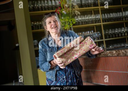 Lächelnde ältere Frau, die eine Geschenkverpackung in einem Geschäft mit Glasregalen im Hintergrund hält. Panc05432 Copyright: XConnectxImagesx Stockfoto