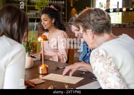 Eine Gruppe von Frauen verschiedenen Alters, die an einem Tisch in einem gemütlichen Restaurant mit Ambiente-Beleuchtung eine Unterhaltung genießen. Panc05471 Copyright: XConnectx Stockfoto