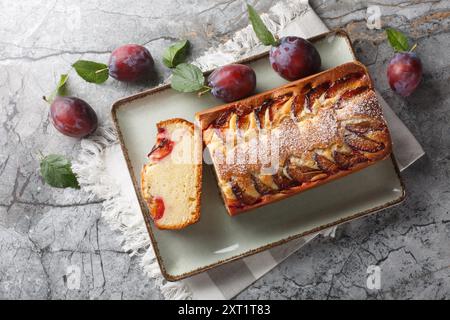 Frisch gebackener Biskuitkuchen mit Pflaumen und Joghurt in Nahaufnahme auf einem Teller auf dem Tisch. Horizontale Draufsicht von oben Stockfoto