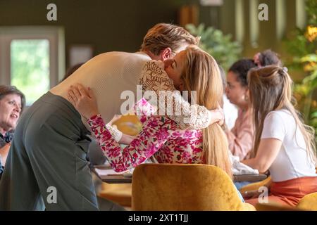 Ein Paar umarmt und küsst sich in einem warmen, sonnendurchfluteten Raum mit Leuten, die an Tischen sitzen. Panc05529 Copyright: XConnectxImagesx Stockfoto