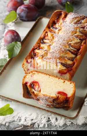 Zarter Biskuitkuchen mit Pflaumen und Joghurt in Nahaufnahme auf einem Teller auf dem Tisch. Vertikal Stockfoto