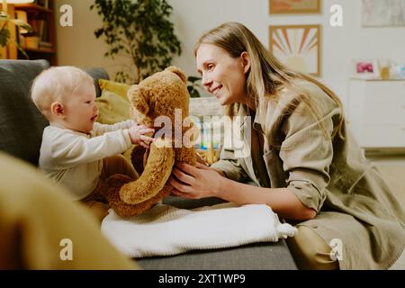 Lächelnde Mutter spielt mit Baby, das Teddybär hält Stockfoto