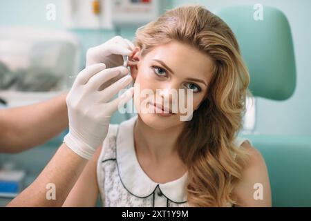 Eine junge Frau sitzt ruhig, während ein Arzt eine Ohrbehandlung in einer hellen Klinik durchführt. Stockfoto