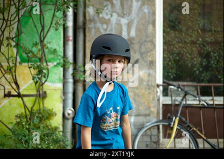 Ein kleines Kind mit Fahrradhelm steht vor einer grünen Kulisse mit einem Fahrrad im Hintergrund. Bola02724 Copyright: XConnectxImagesx Stockfoto