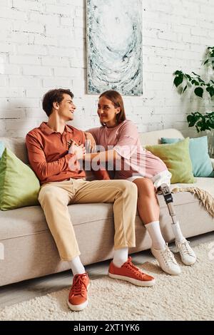 Ein Paar, eine Frau mit einer Beinprothese und ihr Freund, lachen auf einer Couch. Stockfoto