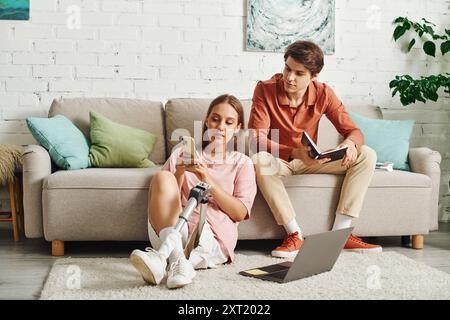 Eine junge Frau mit einer Beinprothese sitzt auf dem Boden, während sich ihr Freund auf der Couch entspannt. Stockfoto