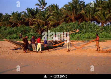 Fischer stehen neben traditionellen Holzfischbooten, die Fischernetze am Induruwa Beach in der Nähe von Bentota, Südprovinz, Sri Lanka sortieren. Archivbild, das 2001 aufgenommen wurde Stockfoto