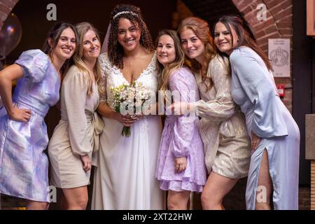 Eine lächelnde Braut in einem weißen Kleid, umgeben von fünf Brautjungfern in pastellfarbenen Kleidern, die sich im Freien posieren. Panc05994 Copyright: XConnectxImagesx Stockfoto