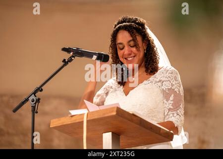 Eine Frau in einem Spitzenkleid lächelt, während sie mit einem Mikrofon aus einer Zeitung liest. Panc06043 Copyright: XConnectxImagesx Stockfoto