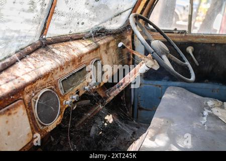 Verlassenes altes, rostiges Auto-Interieur mit Armaturenbrett und Lenkrad, das mit Spinnweben bedeckt ist Stockfoto