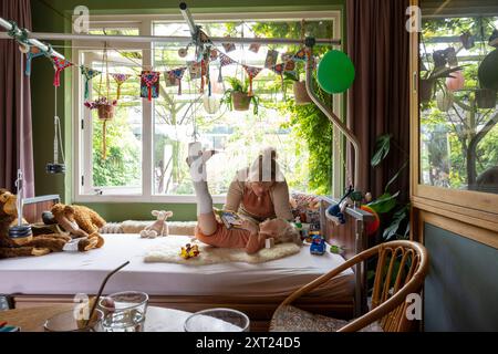 Mutter kümmert sich um ihr verletzte Kind mit Gips an den Beinen. Im Bett liegen und ihnen vorlesen. Panc06162 Copyright: XConnectxImagesx Stockfoto