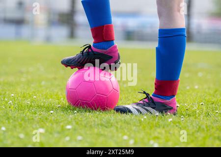 Nahaufnahme der Füße eines Fußballspielers in schwarzen Stollen, die auf einem rosafarbenen Fußball mit einem grünen Rasenfeld im Hintergrund stehen. Panc06294 Copyright: XConn Stockfoto