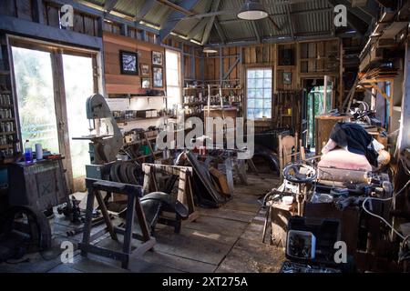 Innenansicht einer rustikalen und überfüllten Holzwerkstatt mit Werkzeugen, Holzdielen und einer Bandsäge, Auckland, Neuseeland, Neuseeland Stockfoto