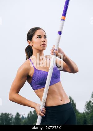 Die Stangenhochspringerin in einem violetten Sport-BH hält ihre Ausrüstung mit Fokus und Entschlossenheit vor einem bewölkten Himmel. Sape00023 Copyright: XConnectxIma Stockfoto