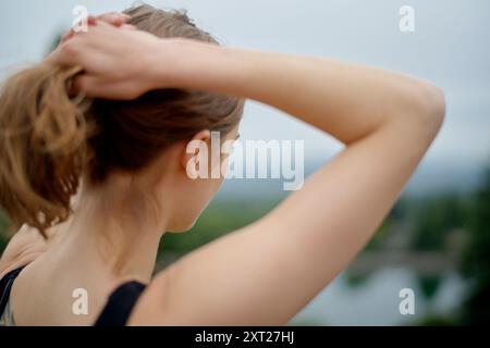 Rückansicht einer Frau, die ihr Haar mit einem verschwommenen natürlichen Hintergrund zusammenbindet. Bola02769 Copyright: XConnectxImagesx Stockfoto