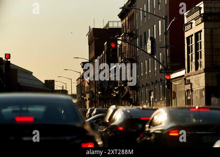 Abendlicher Verkehr auf einer Stadtstraße mit roten Ampeln und der Sonnenuntergang hinter Gebäuden, der ein warmes Leuchten ausstrahlt. Bola02883 Copyright: XConnectxImagesx Stockfoto