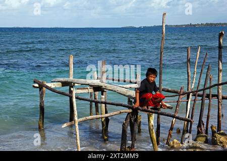 Kuna Boy, der auf einem rustikalen Steg aus Holzpfählen, Stäben und Balken sitzt, Carti Sugtup Island, San Blas Inseln, Panama Stockfoto