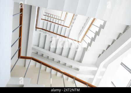 Mit Blick auf eine weiße Wendeltreppe mit Holzgeländern und Metallgeländern entsteht ein abstraktes geometrisches Muster mit Linien und Winkeln. Stockfoto