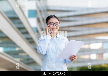 Junger Mitarbeiter, der beim Prüfen von Dokumenten telefonisch in Gespräche eingeht Stockfoto