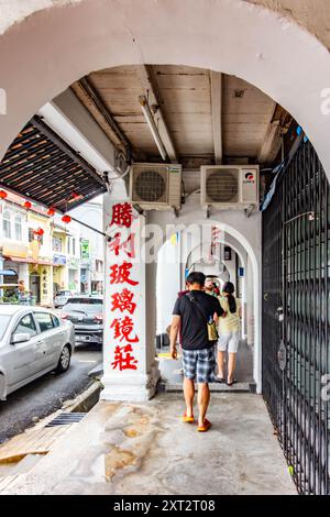 Die Menschen laufen auf einem überdachten Fußweg entlang der Chulia Street in George Town, Penang, Malaysai, durch Bögen und vorbei an chinesischen Schriften. Stockfoto