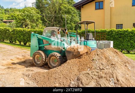 Ein Arbeiter auf einem Skin Loader bewegt Boden, der vor dem Haus ausgehoben wird. Aushubarbeiten und Außenpflaster. Stockfoto