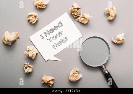 Auf einem Stapel Papier steht eine Lupe, auf der die Worte "Ich brauche deine Hilfe" stehen Stockfoto