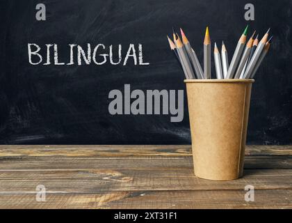 Ein Holztisch mit einer braunen Tasse und einem Haufen Bleistifte. Auf dem Becher steht das Wort zweisprachig Stockfoto