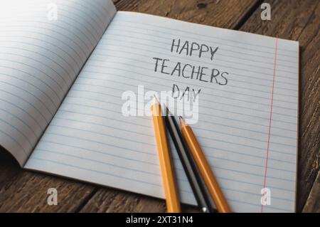 Ein Notizbuch mit Bleistiften und den Worten Happy Teachers Day. Die Stifte werden auf das Notizbuch gelegt, wobei einer auf der linken Seite und einer auf der steht Stockfoto