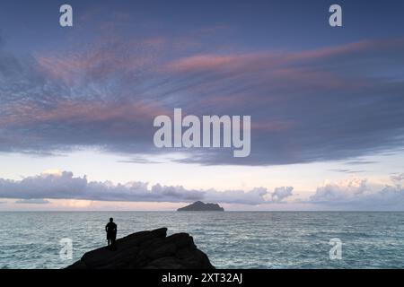 Eine ruhige Küstenlandschaft mit Schildkröteninsel am Horizont. Die Insel ist von einem riesigen blauen Ozean und einem flauschigen Himmel umgeben Stockfoto