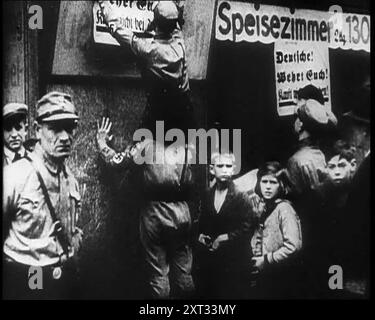 Männer in Nazi-Uniformen, die antijüdische Plakate anbringen, 1933. "Wieder einmal, in der langen Geschichte der Welt, Qualen für die Juden". Aus „Time to Remember – The Time of the Monster“, 1933 (Reel 4); ein Dokumentarfilm über die Ereignisse von 1933, Rise of Roosevelt und Hitler. Stockfoto