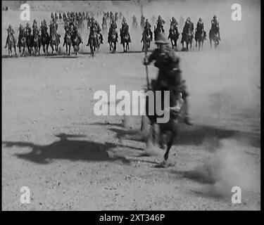 Szene aus einem Film: Schauspieler, die britische Truppen auf dem Pferd auf dem Weg durch eine Wüstenlandschaft spielen, 1920er "Das Fort in Umballa [Ambala], über das die Flagge immer noch flog, der Name des Films spielt keine Rolle, aber eine mutige Anklage brachte diese Situation bald in Ordnung, marschierte in die entlastete Festung, nur um unter den Trümmern nur noch einen Verteidiger zu finden, der am Leben geblieben ist, und den einen, nur einfach." Aus „Time to Remember – Come the Dawn“, 1925 (Reel 3); werfen Sie einen Blick auf die britische Filmindustrie der 1920er Jahre – Clips aus großen Stummfilmen und Wochenschauen. Stockfoto