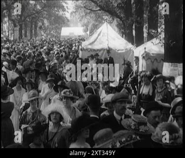 Menschen treffen sich und entspannen auf einem Festplatz zwischen Festzelten und Ballons, 1920. Das Leben kehrt nach dem Ersten Weltkrieg wieder zur Normalität zurück. "Nach vier Jahren düster und khaki... häng die Fahnen und das Fähnchen... du hast dich in Bestform für Royal Ascot oder Lords, und die Eton und Egge, Toppers und das Los... all das war viel besser als Ypern oder die Somme." Aus "Time to Remember - the Plunge into Peace", 1920 (Reel 1); Ereignisse von 1920 - Hochzeiten, Frauenrechte, industrielle Unruhen und Probleme in Irland. Stockfoto