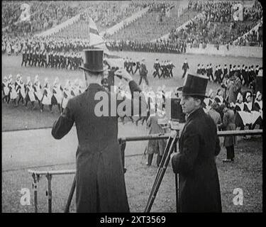 Männliche Newsreel Kamerabediener mit Stativen und Ausrüstung, 1920er Jahre "...die britische Empire-Ausstellung in London 1924 - das war die große Demonstration von Einheit und Ressourcen, die zur Förderung der Solidarität des Imperiums und zur Förderung des Handels genutzt wurden. So großartig waren einige seiner Funktionen, dass viele Kameramänner in Spitzenhüten und Morgenkleidern auftauchten, um ihre Griffe zu drehen. Aus „Time to Remember – Come the Dawn“, 1925 (Reel 3); werfen Sie einen Blick auf die britische Filmindustrie der 1920er Jahre – Clips aus großen Stummfilmen und Wochenschauen. Stockfoto