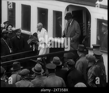 Die Partei von Mohandas K Gandhi (Mahatma) landet in London Docks für eine der Runden Tischkonferenzen (Indien), 1931. In einen britischen Hafen segelte jemand, dessen Kleidung und Verhalten ihn zur am meisten verbreiteten Figur der Zeit machten. In London wurde ein Rundtischgespräch einberufen, um die heiklen Probleme Indiens und ihre Forderungen nach Selbstbestimmung in Frieden zu regeln. In London erschien also das lebendige Symbol von unzähligen Millionen, Mahatma Gandhi. Aus „Time to Remember – A New Era“, 1931 (Reel 1); Dokumentarfilm über die Welt in den frühen 1930er Jahren Stockfoto