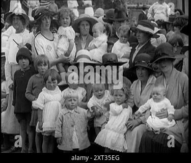 Britische Mütter sitzen mit ihren Babys auf dem Schoß bei einer Baby Show, 1920. Großbritannien kehrt nach dem Ersten Weltkrieg zur Normalität zurück. „Ein Frieden, all diese Kinder zu haben, die man so lange aufgeschoben hat, bis man das Gefühl hatte, dass die Welt für sie sicher ist“. Aus "Time to Remember - the Plunge into Peace", 1920 (Reel 4); Ereignisse von 1920 - Hochzeiten, Frauenrechte, industrielle Unruhen und Probleme in Irland Stockfoto