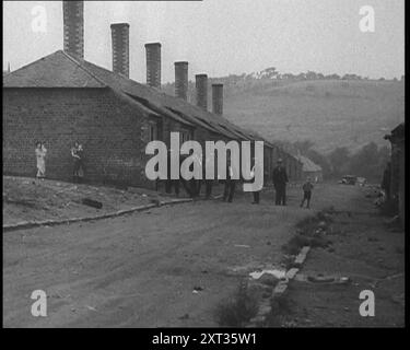 Gruppe von Männern, Frauen und Kindern, die auf einer Straße herumstehen, 1933. Die große Depression in Großbritannien. „In [den] schwer getroffenen Tälern von Wales und auf Clydebank und Jarrow gingen die Regierungsvergaben nicht weit.“ Aus „Time to Remember – The Time of the Monster“, 1933 (Reel 3); ein Dokumentarfilm über die Ereignisse von 1933, Rise of Roosevelt und Hitler. Stockfoto