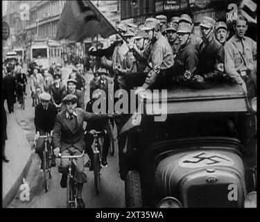 Gruppe von Männern in Nazi-Uniform, die die Straße hinunterfahren, wie Zivilisten beobachten, 1933. "Wieder einmal, in der langen Geschichte der Welt, Qualen für die Juden". Aus „Time to Remember – The Time of the Monster“, 1933 (Reel 4); ein Dokumentarfilm über die Ereignisse von 1933, Rise of Roosevelt und Hitler. Stockfoto