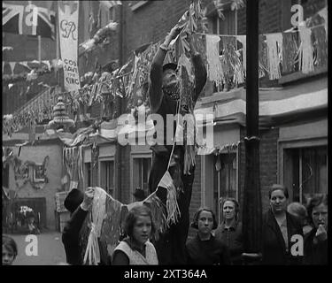 Mann, der Bunting von einem Lampenkopf in einer Straße mit Dekorationen für die Krönung von George VI., 1937 hängt. Ein Anlass, der nicht sehr oft kommt. Wenn es das tut, machen Sie das Beste daraus. Und wie sehr man daraus eine Party macht, hängt ganz von Ihrem Wertegefühl ab. Also machte sich Großbritannien bereit." Aus "Time to Remember - Sense of Values", 1937 (Reel 1); Dokumentarfilm über die Ereignisse von 1937, Krieg im Fernen Osten, Aufbau bis Krieg in Europa. Stockfoto