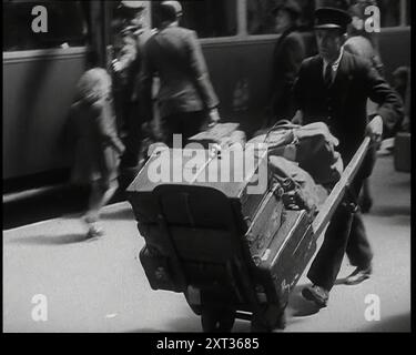 Ein männlicher Bahnhofsträger schiebt eine Sackkarre mit Koffern und Taschen auf einem Bahnsteig mit einem Zug hinter ihm, 1938. Aus „Time to Remember – Wind Up Week“, 1938 (Reel 2); Dokumentarfilm über 1938 – die Menschen werden sich der wachsenden Bedrohung des Krieges bewusst. Stockfoto