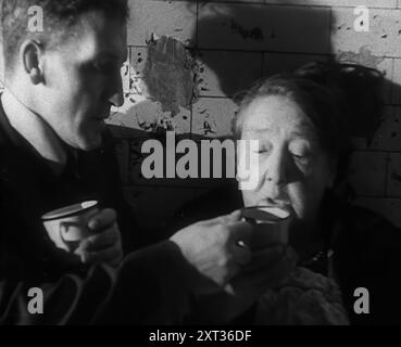 Zivilisten trinken heiße Getränke, während sie vor Bomben geschützt sind, in der Londoner U-Bahn, 1940. Großbritannien während des Zweiten Weltkriegs: Menschen, die sich vor dem Londoner Blitz schützen. „Unter der größten Stadt der Welt lässt sich ein Gastgeber nieder, tief vor der furchtbaren Nacht [dh deutsche Bombenangriffe]. Höhlen für Menschen weg von den Bomben und einem Stahlregen von den wohlmeinenden Waffen. Ist das nicht das Teetablett? Also wach auf, Mrs. Higgins von Bethnal Green, Tee ist auf Enten. Trink es, solange es schön heiß ist. Aus „Time to Remember – Standing Alone“, 1940 (Reel 4); Dokumentarfilm f Stockfoto