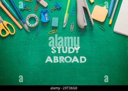 Eine grüne Tafel mit einem Haufen Bürobedarf und dem Wort „Auslandsstudium“. Zu den Verbrauchsmaterialien gehören Scheren, Stifte und ein Hefter Stockfoto
