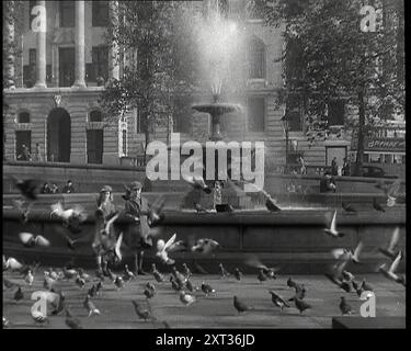 Ein Junge und ein Mädchen füttern Tauben an einem der Springbrunnen am Trafalgar Square mit Fußgängern, einem Bus und Südafrika Haus sichtbar im Hintergrund, 1939. Aus „Time to Remember – The Reluctant Warriors“, 1939 ( Reel 2); Dokumentarfilm über Ereignisse von 1939 – Vorbereitungen für den Krieg und dann Feindseligkeiten brechen aus. Stockfoto