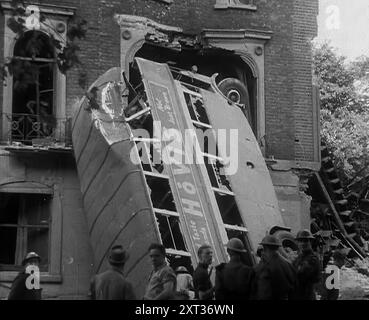 Leute stehen neben einem bombardierten Bus, 1940. Großbritannien während des Zweiten Weltkriegs: Der Blitz. "Jede Nacht, zu jeder Zeit, Sommer 1940. Feuer und Flamme, Tod und Zerstörung... jeden Morgen danach in London - oder ist es Coventry, Bristol, Portsmouth? Liverpool, Belfast, Birmingham? Plymouth oder Glasgow? Löcher, wo gestern keine Löcher waren, keine Häuser, wo die Häuser von gestern waren. Defekte Netzleitungen spritzen Wasser, Abwasser, Gas oder Feuer. Unter den Füßen das Knirschen von zersplittertem Glas, als würde man an einem Kiesstrand spazieren gehen. Kein Wunder, dass ich heute Morgen keine Nummer 15 bekam. Aus "Zeit Bis Zur Erinnerung - Standing Al Stockfoto