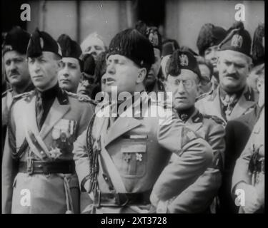 Benito Mussolini, der italienische Führer, hielt eine Rede und stand mit den Händen auf den Hüften vor einer Menge uniformierter männlicher italienischer faschistischer Beamter, 1939. Aus „Time to Remember – The Reluctant Warriors“, 1939 (Reel 1); Dokumentarfilm über Ereignisse von 1939 – Vorbereitungen für den Krieg und dann Feindseligkeiten brechen aus. Stockfoto