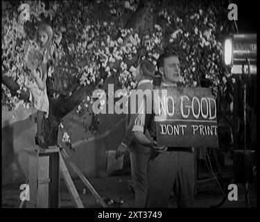 Weibliche Schauspielerin sitzt in einem Blossom Tree, während ein männlicher Zivilist mit ihr spricht. Ein Filmtechniker hält eine Klapptafel mit der Aufschrift „No Good, Don't Print“, 1920er Jahre Elstree, im Großen und Ganzen das Hollywood Großbritanniens in den Zwanzigern, aber ohne Palmen und Sonne. Aber auf den Bühnen mit Zinndach konnte man es zu jeder Jahreszeit schaffen. Aus „Time to Remember – Come the Dawn“, 1925 (Rolle 1); werfen Sie einen Blick auf die britische Filmindustrie der 1920er Jahre – Clips aus großen Stummfilmen und Wochenschauen. Stockfoto