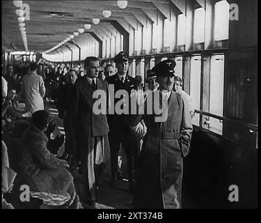 Adolf Hitler, der deutsche Führer, ging mit dem deutschen Offizier und anderen, darunter Robert Ley, einen langen Korridor hinunter und grüßte, auf einem Deck des Kreuzfahrtschiffes „Kraft durch Freude“, der Robert Ley, 1939. Aus „Time to Remember – The Reluctant Warriors“, 1939 (Reel 1); Dokumentarfilm über Ereignisse von 1939 – Vorbereitungen für den Krieg und dann Feindseligkeiten brechen aus. Stockfoto