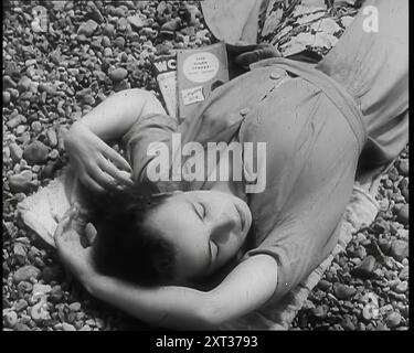 Eine junge Frau, die am Strand in Brighton liegt, mit geschlossenen Augen, mit zwei Büchern an der Seite von ihr, einer davon ist die Dark Street von Peter Cheyney, 1939. Aus „Time to Remember – The Reluctant Warriors“, 1939 (Reel 1); Dokumentarfilm über Ereignisse von 1939 – Vorbereitungen für den Krieg und dann Feindseligkeiten brechen aus. Stockfoto