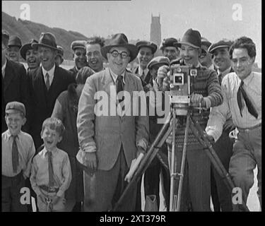 A Group of People laghing as they are (eine Gruppe lachender Menschen, wie sie sind) Sehen Sie sich den Film, der von hinter einer Kamera gedreht wird, 1920er Jahre an Drehort. "Elstree [Filmstudios] in den Tagen der Stille... als das Wetter schön war, gingen wir in die Sonne hinaus." Aus „Time to Remember – Come the Dawn“, 1925 (Rolle 1); werfen Sie einen Blick auf die britische Filmindustrie der 1920er Jahre – Clips aus großen Stummfilmen und Wochenschauen. Stockfoto