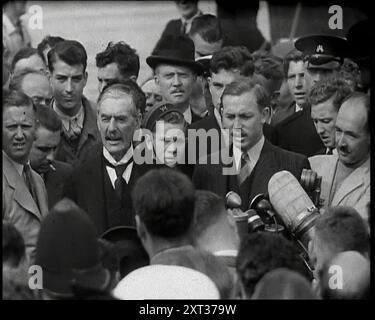 Neville Chamberlain, der britische Premierminister, sprach mit männlichen Journalisten und Mitgliedern der Öffentlichkeit auf dem Heston-Flugplatz, nachdem er 1938 von einem Treffen mit Adolf Hitler, dem deutschen Führer, in München zurückgekehrt war. Aus „Time to Remember – Wind Up Week“, 1938 (Reel 3); Dokumentarfilm über 1938 – die Menschen werden sich der wachsenden Bedrohung des Krieges bewusst. Stockfoto