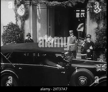 Adolf Hitler, der deutsche Führer, der aus einem Gebäude in Bad Godesburg mit männlichen deutschen Beamten und Gardisten bei der Begrüßung des britischen Premierministers Neville Chamberlain, der auf der Rückseite eines Autos sitzt, 1938. Aus „Time to Remember – Wind Up Week“, 1938 (Reel 3); Dokumentarfilm über 1938 – die Menschen werden sich der wachsenden Bedrohung des Krieges bewusst. Stockfoto